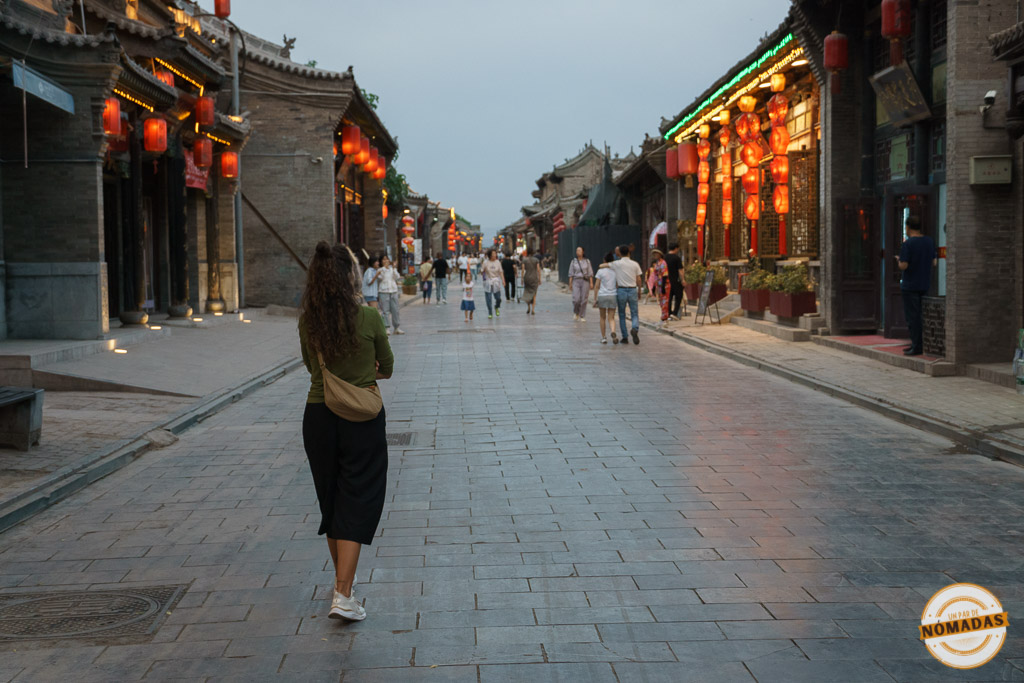 Tatiana caminando al atardecer por una calle tradicional de Pingyao, con faroles rojos iluminando el ambiente