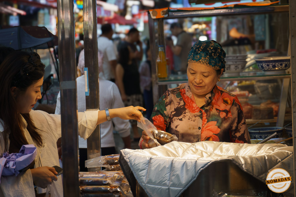 Mujer con pañuelo atendiendo un puesto de comida callejera en el barrio musulmán de Xi’an, mientras una clienta realiza una compra