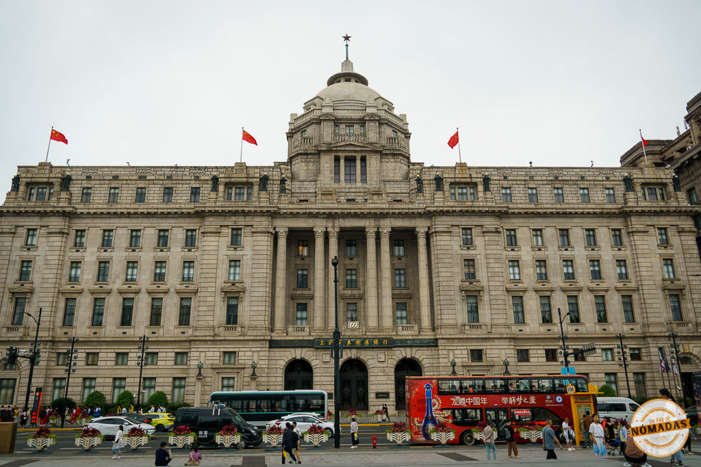 Fachada de edificios históricos de estilo neoclásico en el Bund de Shanghái, China, con banderas chinas y tráfico urbano
