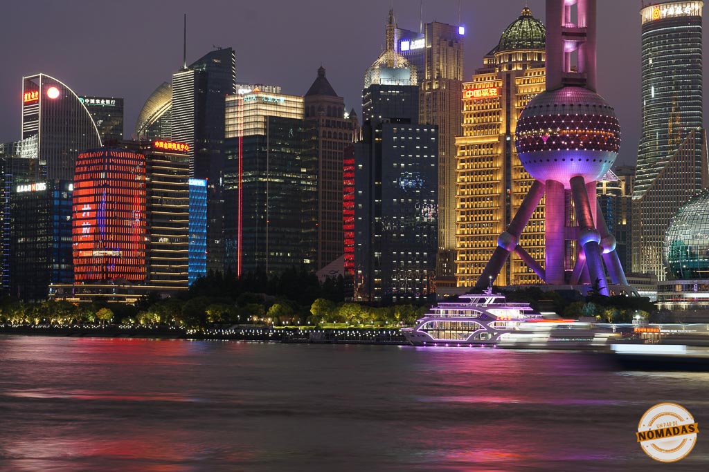 Barco iluminado navegando por el río Huangpu al anochecer, con los rascacielos del Bund de Shanghái reflejados en el agua
