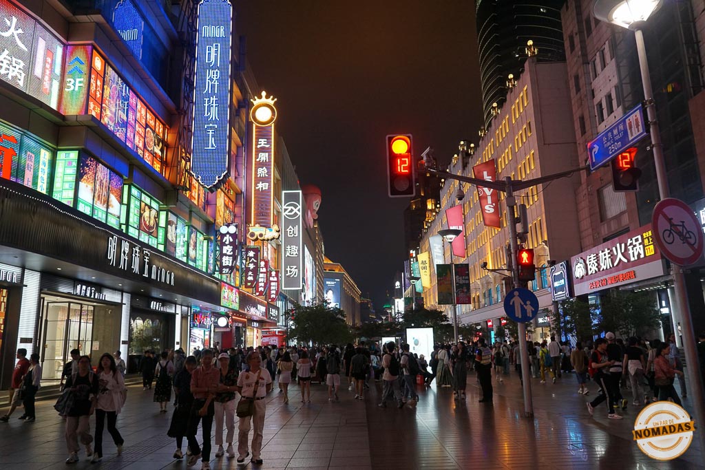 Vista nocturna de Nanjing Road en Shanghái con multitud de viandantes y letreros luminosos de tiendas
