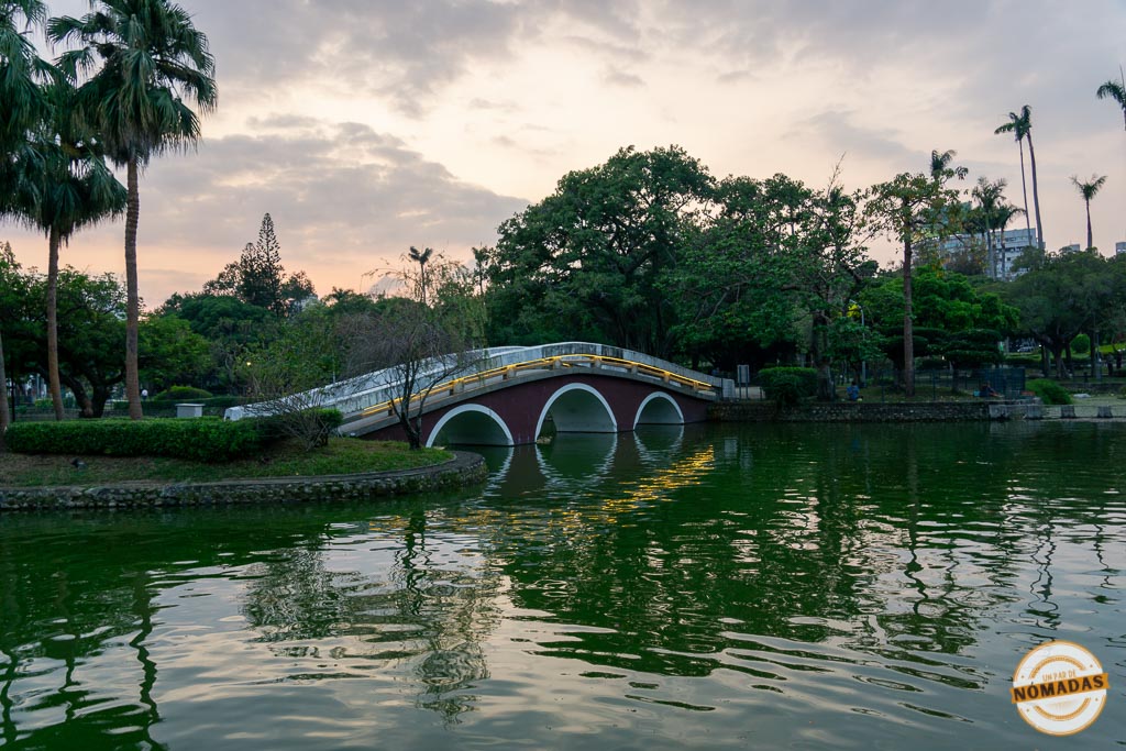 Puente curvo sobre lago rodeado de vegetación en el Taichung Park