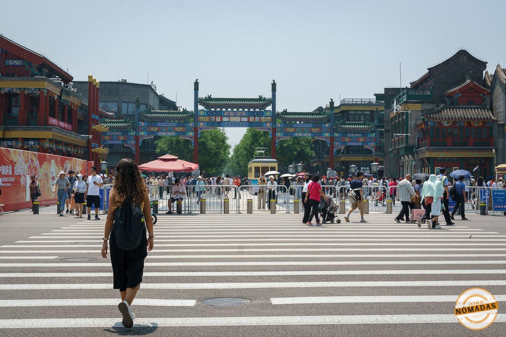 Qué ver en la Calle Qianmen de Pekín: turista cruzando un paso de peatones con el arco tradicional de Qianmen al fondo y tranvía histórico