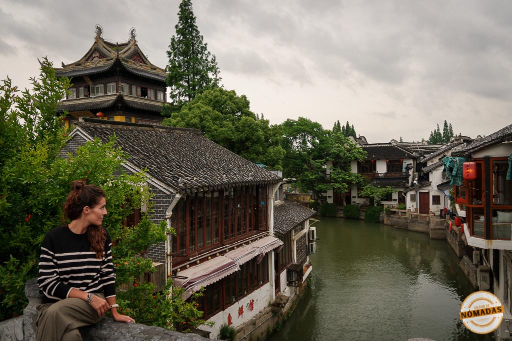 Tatiana sentada junto al canal de Zhujiajiao rodeada de casas tradicionales de madera y puentes antiguos en el famoso pueblo acuático de China
