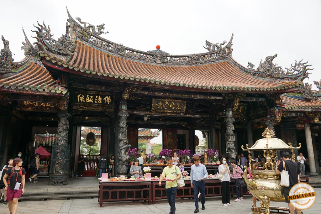 Entrada principal del Longshan Temple en Taipéi con visitantes, ofrendas florales y detalles arquitectónicos tradicionales decorados con dragones.