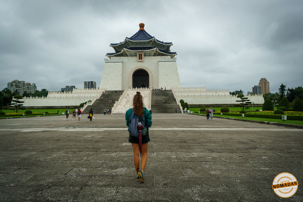 Tatiana caminando hacia el monumental Memorial de Chiang Kai-shek en Taipéi, con cielo nublado y jardines simétricos alrededor.