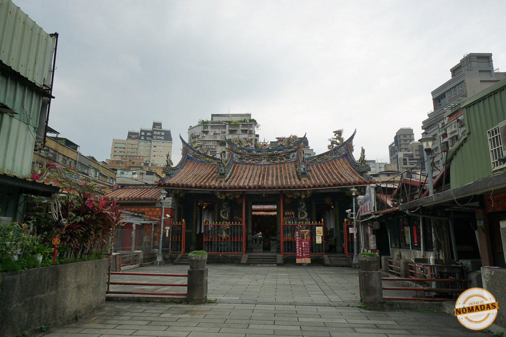 Fachada del Qingshui Temple en Taipéi, con techos ornamentados, columnas talladas y edificios modernos en el fondo.
