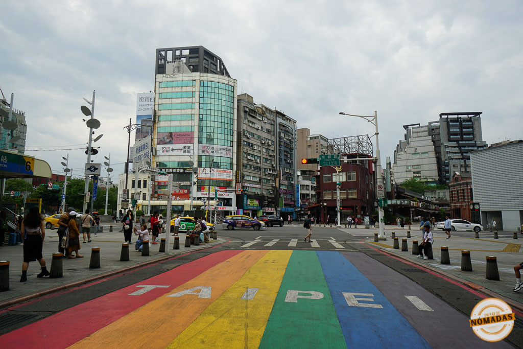 Paso peatonal arcoíris con la palabra Taipéi pintada, rodeado de edificios comerciales y transeúntes en el barrio de Ximending.