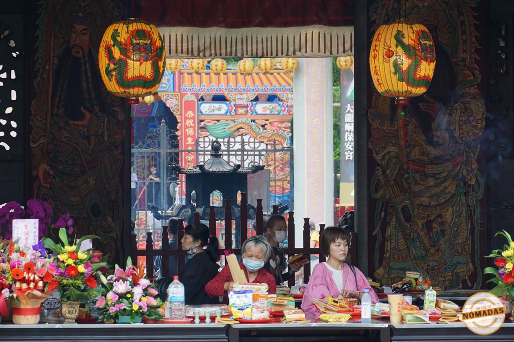 Mujeres realizando ofrendas tradicionales en el templo Dalongdong Baoan de Taipéi, rodeadas de faroles, flores y símbolos religiosos.