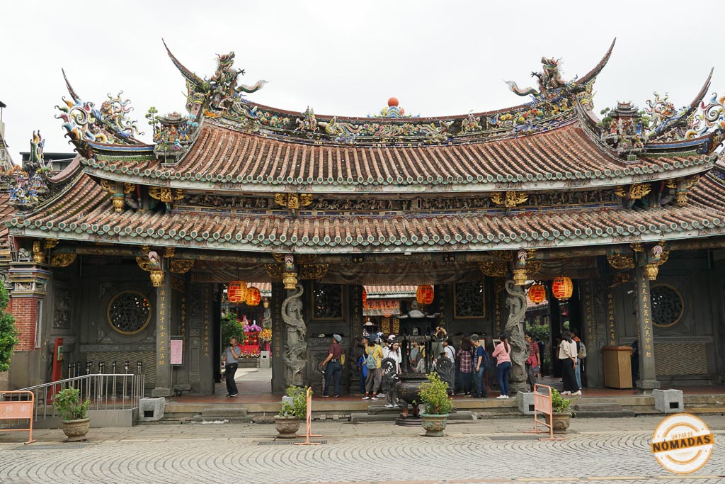 Fachada principal del templo Xingtian en Taipéi, con visitantes realizando rituales y decoraciones talladas en techos y columnas.