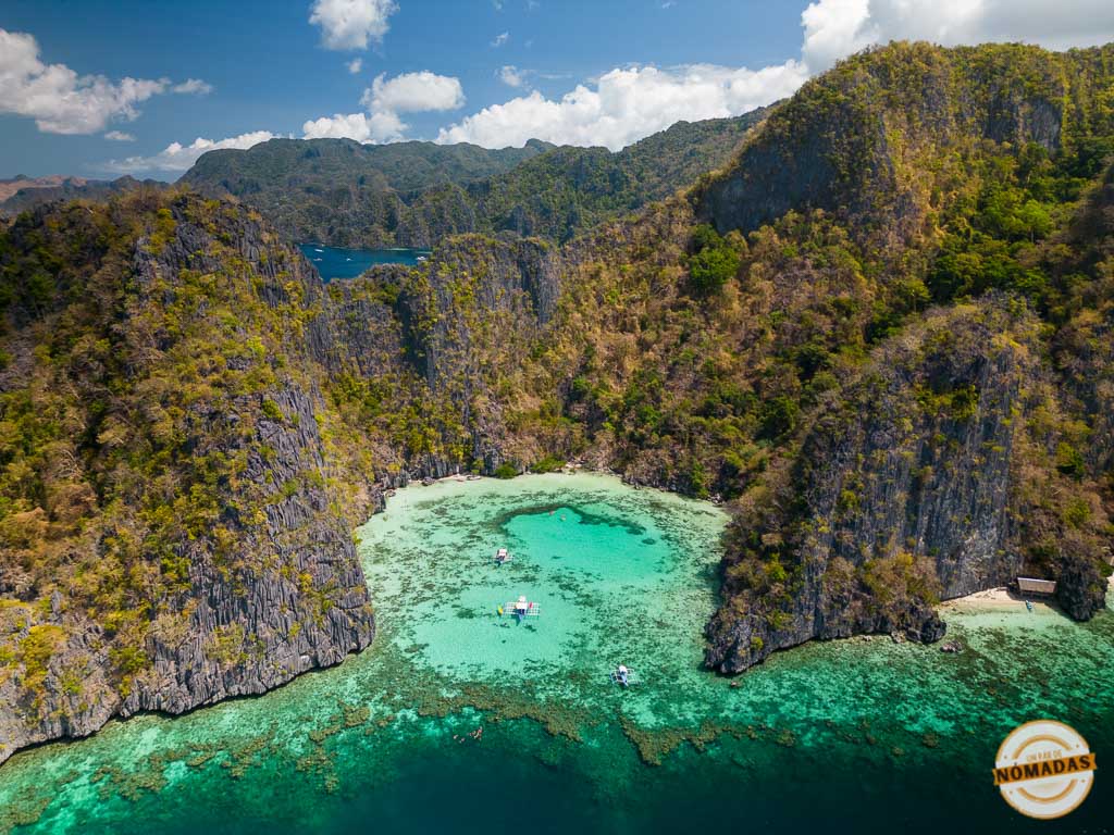 Vista aérea de una laguna turquesa rodeada de corales y formaciones rocosas en Coron, Palawan, con pequeñas bancas flotando cerca.