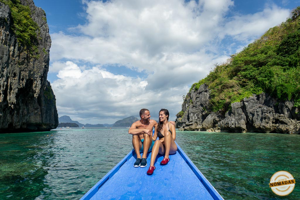Pareja sentada en la proa de una banca tradicional filipina sobre aguas cristalinas, rodeados de acantilados en El Nido, Palawan.