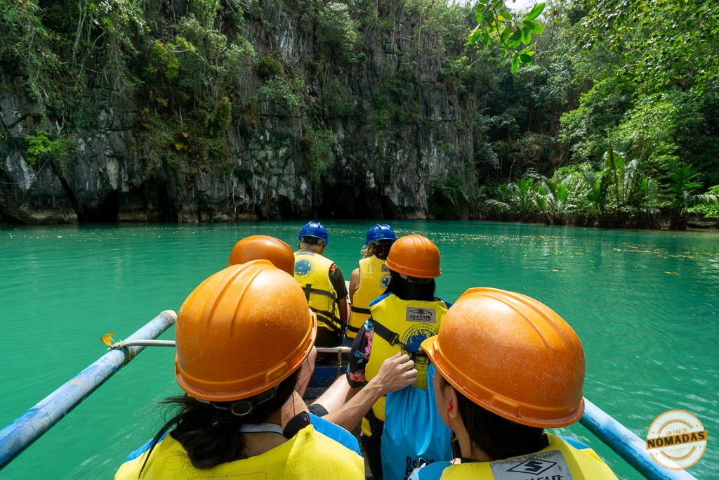 Grupo con cascos y chalecos salvavidas navegando en bote por el río subterráneo de Puerto Princesa, rodeado de selva tropical y formaciones rocosas, en Filipinas.