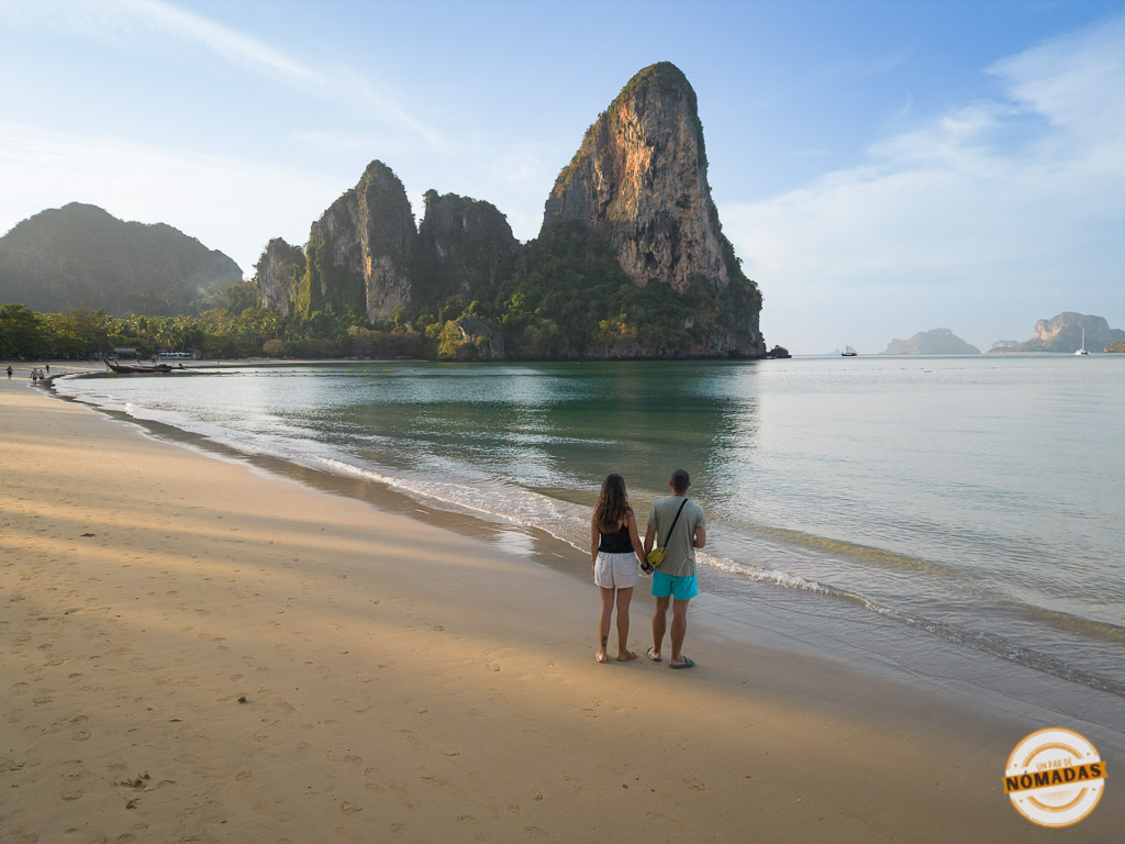 Oscar y Tatiana caminando por la playa de Railay, en Krabi, Tailandia, con el icónico acantilado al fondo y mar en calma