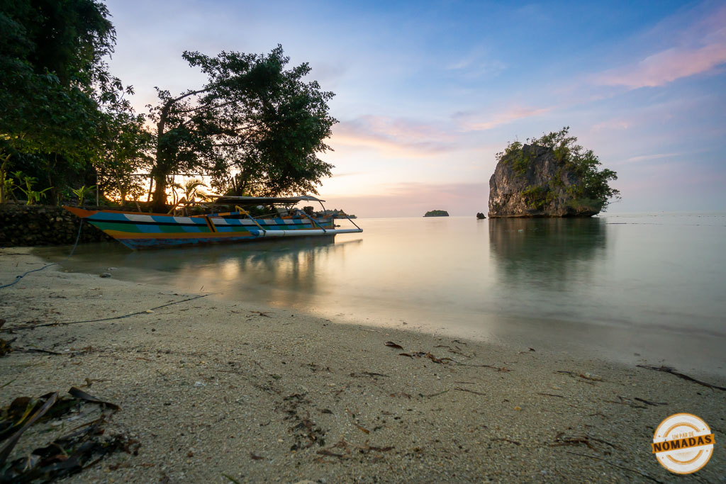 Barca tradicional en la orilla de Kadidiri al atardecer, con islotes y cielo rosado en Sulawesi, Indonesia