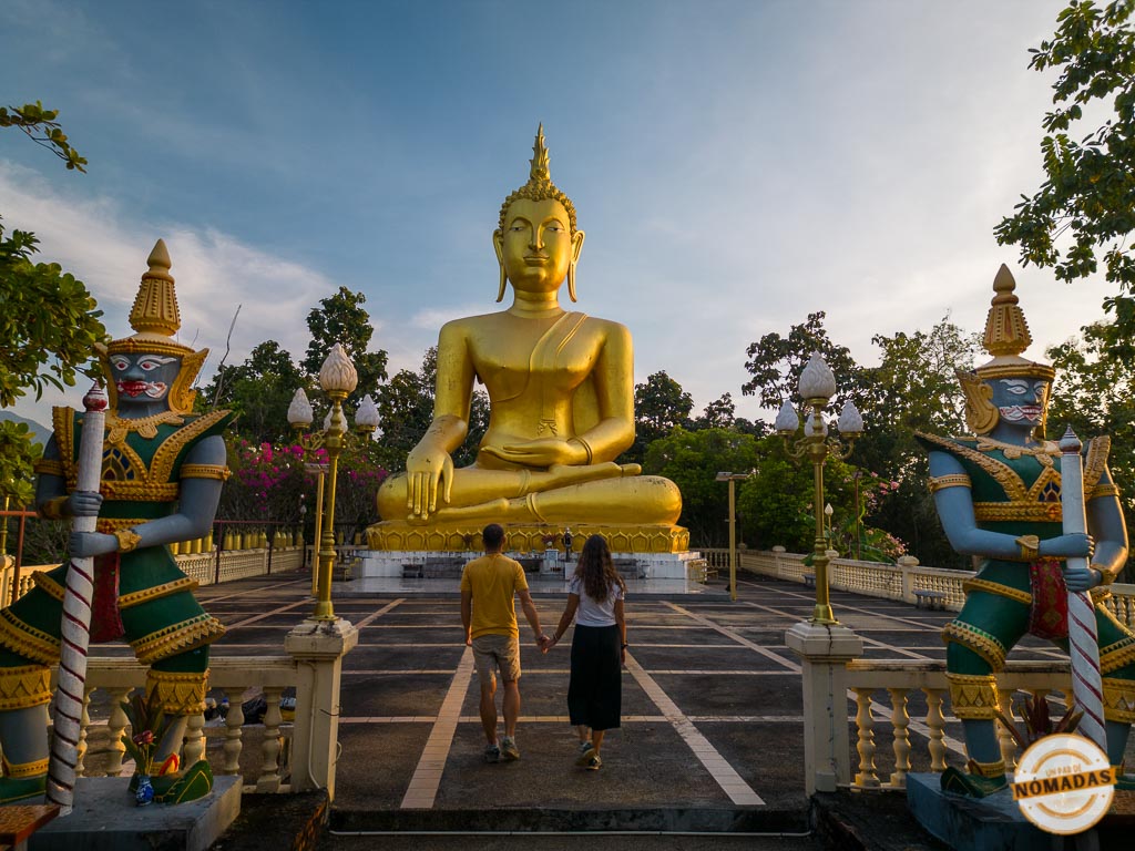 Oscar y Tatiana camina hacia gran estatua dorada flanqueada por guardianes en Wat Chom Thong