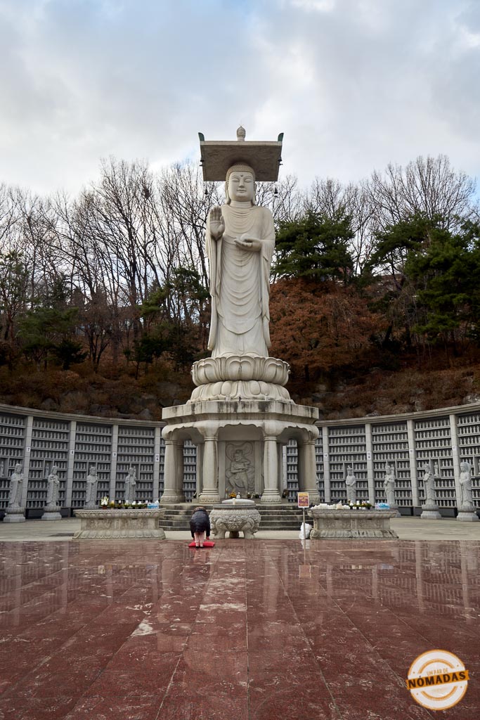 Gran estatua de Buda con ofrendas y una persona orando en el Templo Bongeunsa de Seúl