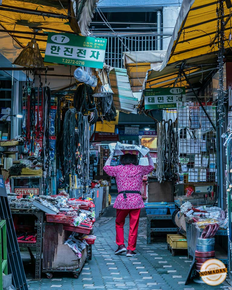 Mujer con ropa colorida cargando objetos en un estrecho pasillo del mercado de Dongmyo en Seúl