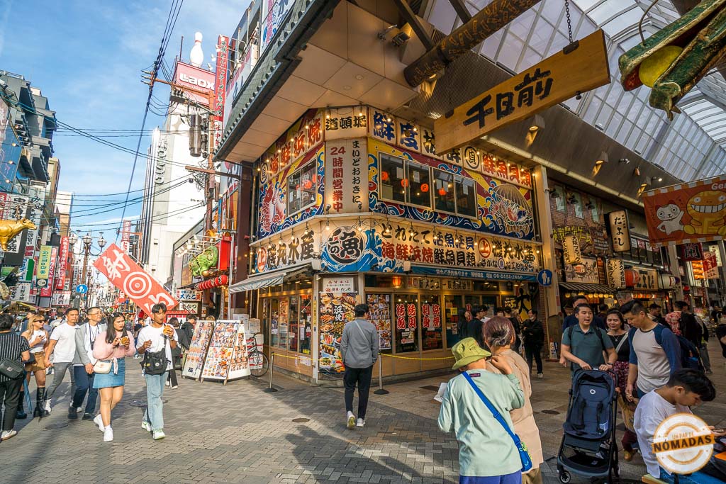 Calle comercial llena de carteles, restaurantes y personas. Uno de los mejores lugares que visitar en Osaka