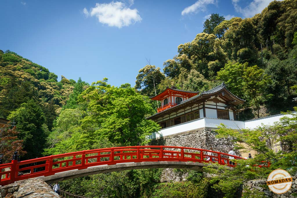 Templo japonés sobre una colina con puente rojo rodeado de vegetación.

