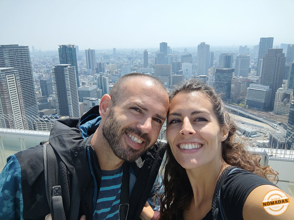 Pareja sonriente en el mirador del Umeda Sky Building con la ciudad de Osaka al fondo en un día despejado
