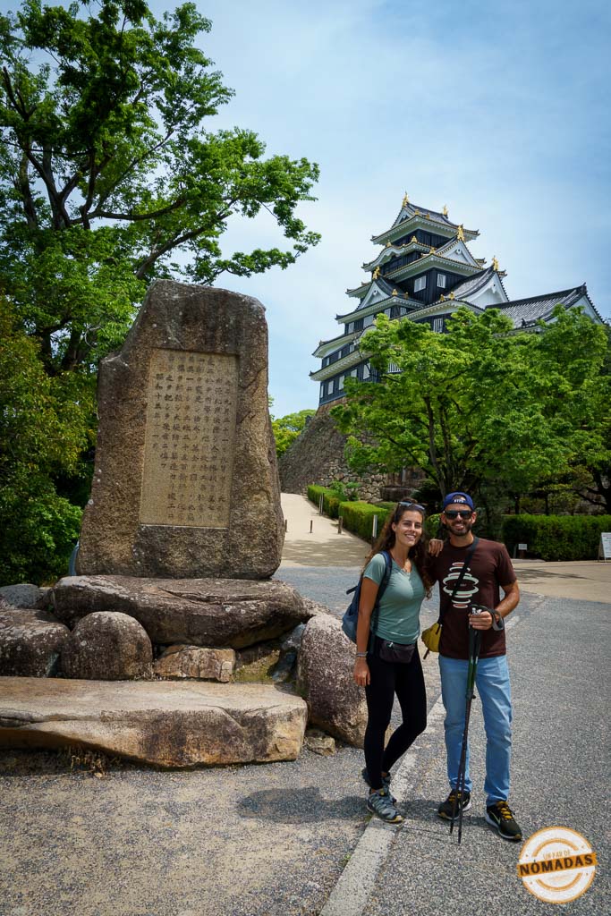 Pareja viajera frente al castillo de Okayama junto a una piedra con inscripción