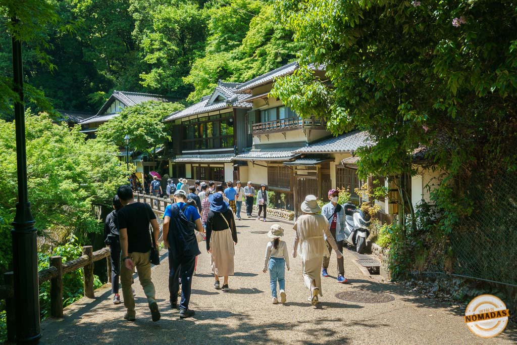 Turistas caminando entre árboles y construcciones tradicionales en el parque Minoh. Una excursión desde Osaka
