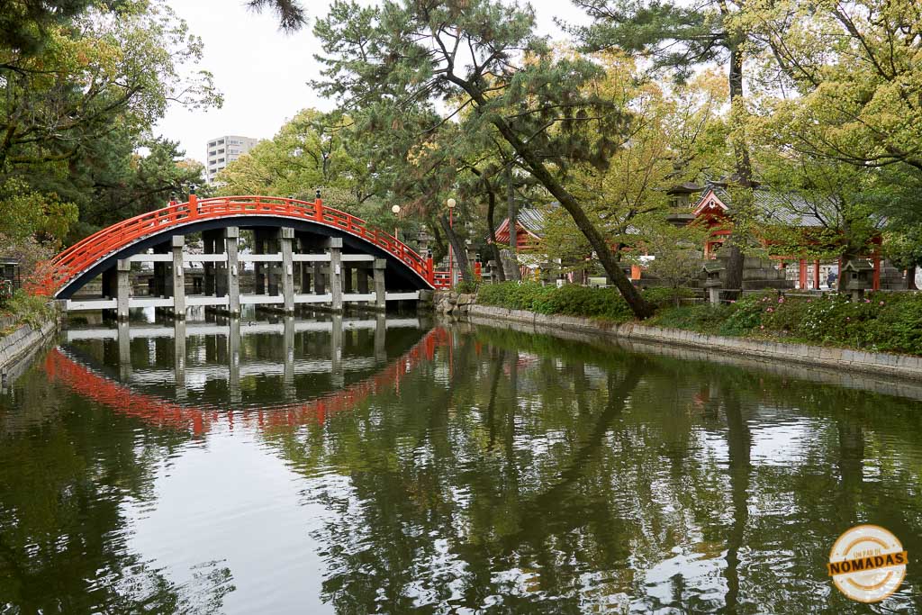 Puente Sorihashi de arco rojo reflejado en el estanque del santuario Sumiyoshi Taisha de Osaka, rodeado de vegetación
