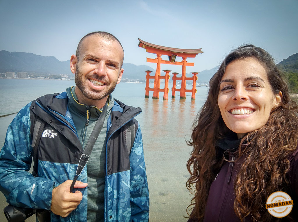 Selfie de un par de nómadas sonrientes frente al torii flotante del santuario Itsukushima en Miyajima