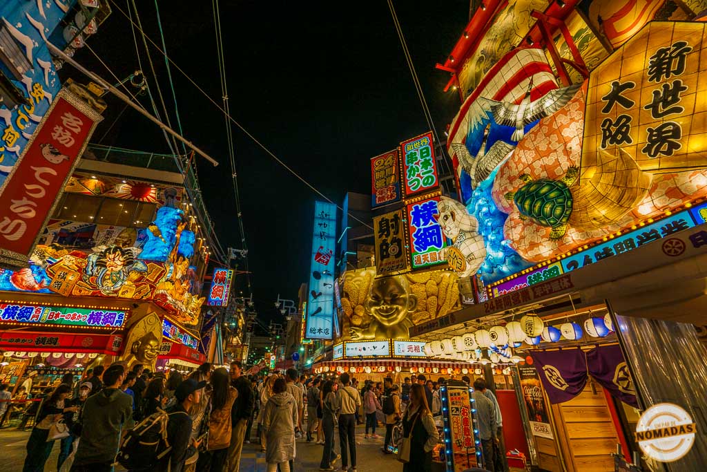 Calle del barrio Shinsekai en Osaka llena de luces de neón, farolillos y carteles tradicionales, con mucha gente paseando de noche
