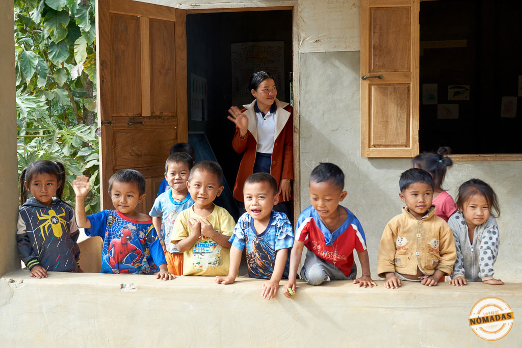 Grupo de niños sonrientes y una maestra saludando en una escuela de una aldea local
