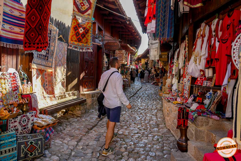 Hombre caminando por la calle adoquinada del Bazar Antiguo de Krujë, Albania, rodeada de tiendas de artesanía local y alfombras.