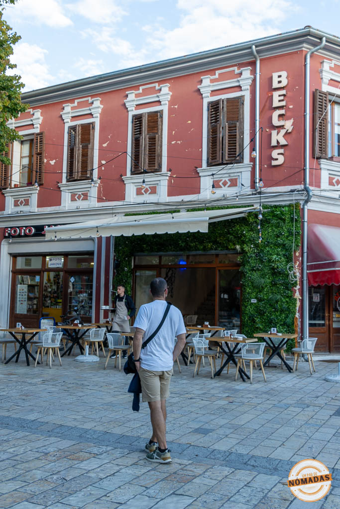 Hombre paseando frente a un edificio rojo con terrazas en la calle peatonal Kolë Idromeno, en el centro de Shkodër.