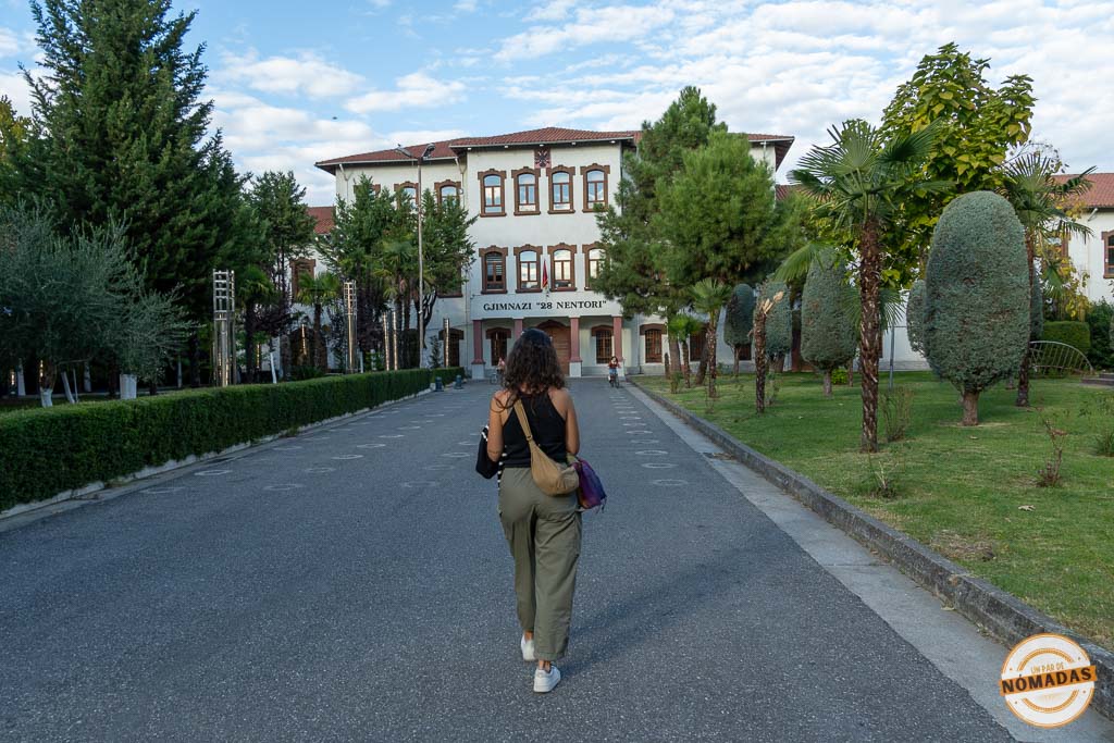Mujer caminando hacia el edificio del Gjimnazi 28 Nëntori en Shkodër, ilustrando lo fácil y seguro que es moverse a pie por la ciudad.