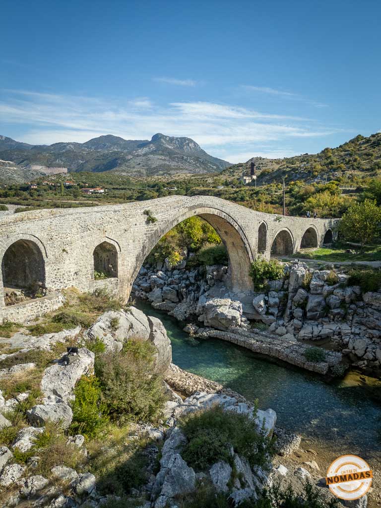 Vista vertical del Puente de Mes (Ura e Mesit) cruzando el río Kir, destacando su arquitectura otomana y el paisaje montañoso de Shkodër.