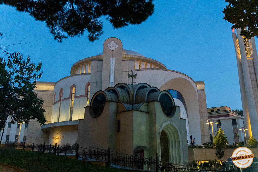 Vista nocturna de la Catedral Ortodoxa de la Resurrección de Cristo en Tirana iluminada, con su gran cúpula y campanario separado.
