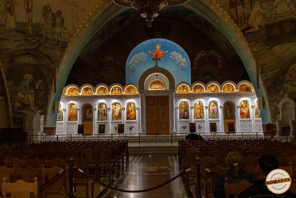 Interior de la Catedral Ortodoxa de la Resurrección de Cristo en Tirana, mostrando el iconostasio dorado iluminado y los grandes frescos en las paredes.