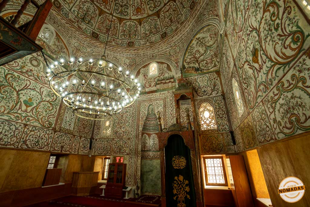Interior de la Mezquita de Et'hem Bey en Tirana, mostrando la cúpula decorada con lámparas y frescos coloridos de motivos vegetales.