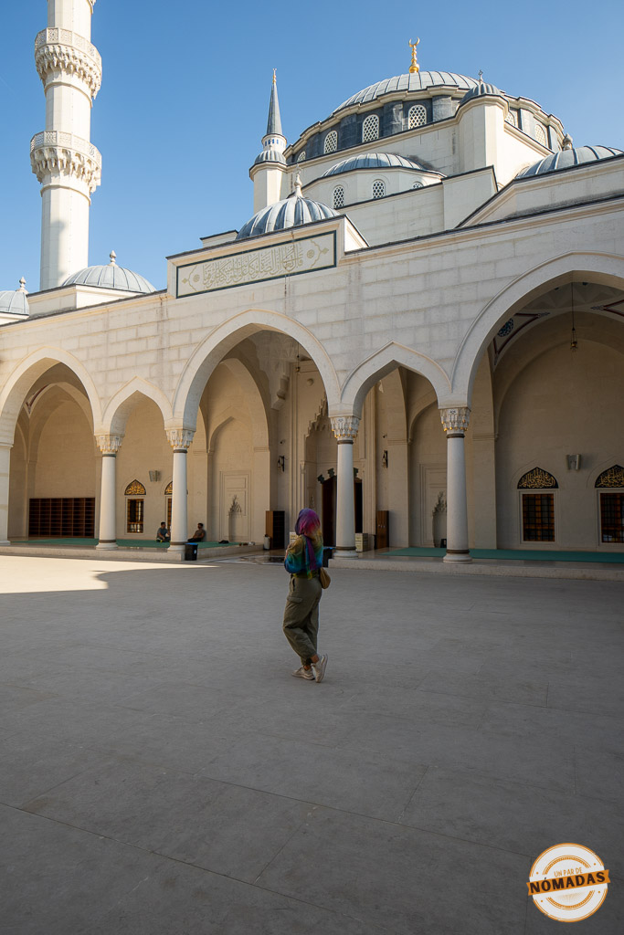 Tatiana observando la arquitectura del patio interior de la Gran Mezquita de Namazgah, con arcos blancos y cúpulas bajo el cielo azul.