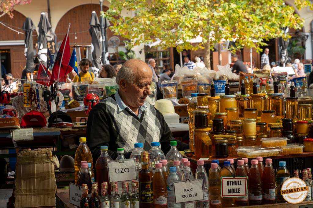 Vendedor local en su puesto del mercado Pazari i Ri de Tirana, con botellas de raki casero, uzo y tarros de miel.