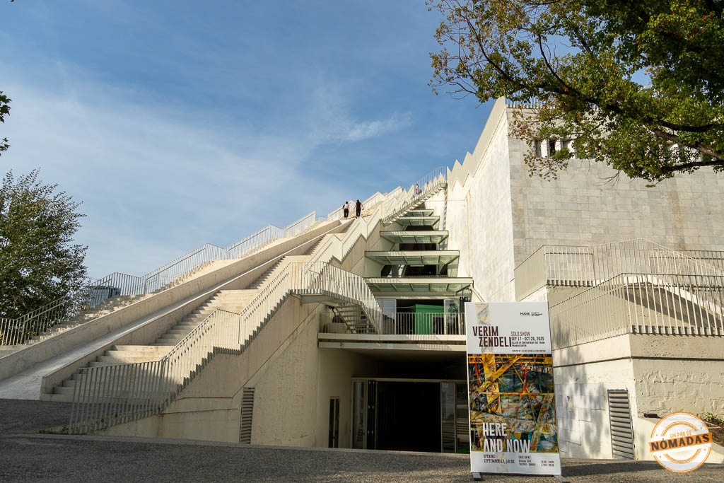 Fachada lateral de la Pirámide de Tirana con escaleras exteriores y un cartel de exposición de arte moderno en la entrada.
