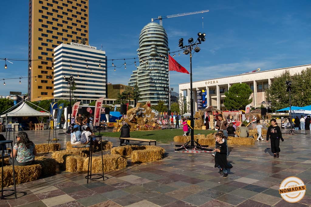 Familias y niños disfrutando de un evento al aire libre en la Plaza Skanderbeg, con el rascacielos Eyes of Tirana y la Ópera de fondo.