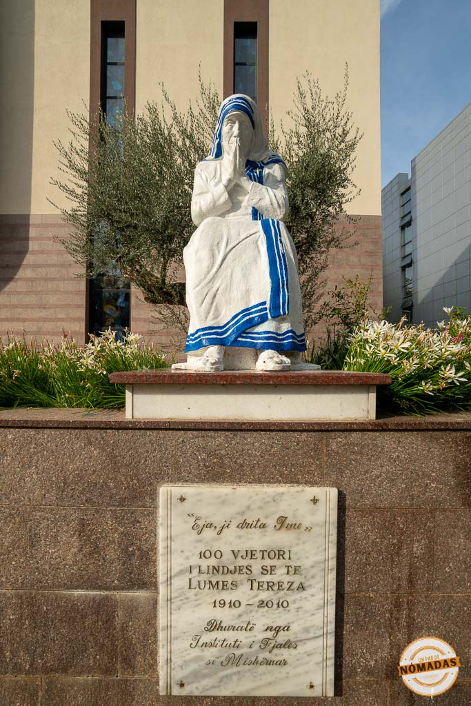 Estatua blanca de la Madre Teresa de Calcuta sentada en posición de oración, con una placa conmemorativa en el centro de Tirana.