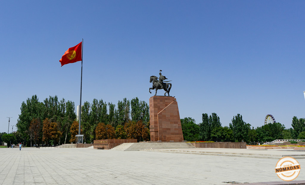 Gran explanada pavimentada de la Plaza Ala-Too con la enorme bandera roja de Kirguistán ondeando al viento junto a la estatua ecuestre del héroe Manas, símbolos que ver en Bishkek