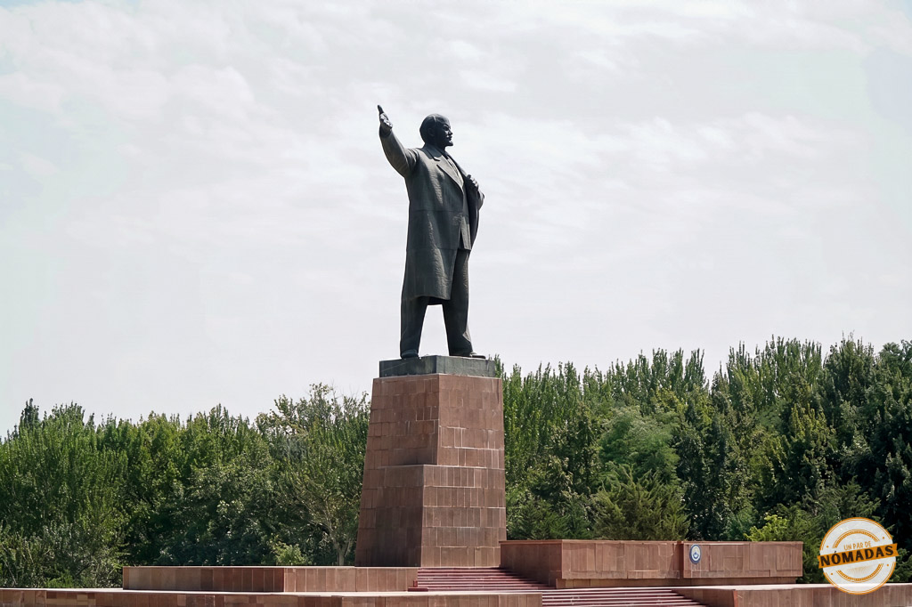 Imponente estatua de bronce de Lenin con el brazo en alto sobre un gran pedestal rojizo, un importante monumento histórico que ver en Bishkek