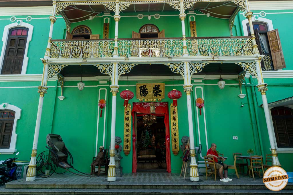 Fachada exterior de color verde menta de la histórica Pinang Peranakan Mansion en Georgetown, destacando sus elegantes balcones de hierro forjado blanco y dorado y farolillos rojos en la entrada.