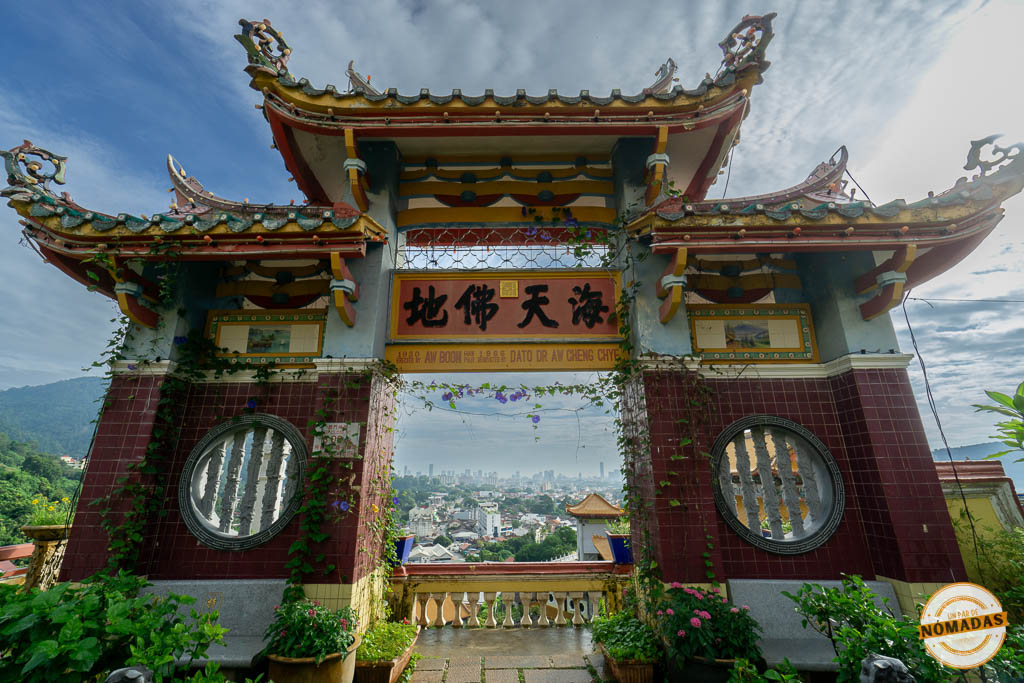 Arco tradicional chino decorado con enredaderas y flores moradas enmarcando una vista panorámica de la ciudad de Georgetown desde las montañas de Penang.