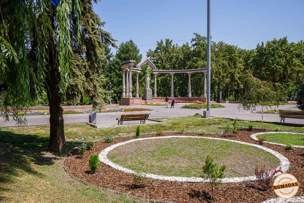 Jardines soleados y caminos pavimentados que conducen a un gran monumento de piedra con columnas en el Parque Panfilov, un tranquilo espacio verde que ver en Bishkek