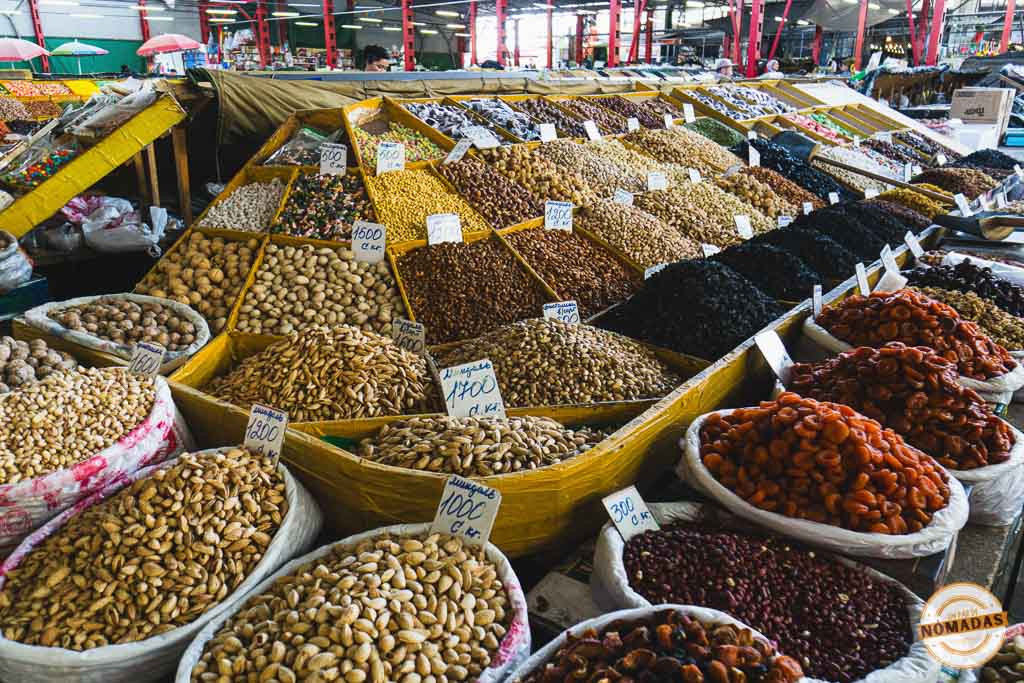 Mostrador del Osh Bazar repleto de enormes montañas de frutos secos, nueces y albaricoques deshidratados con etiquetas de precios, una experiencia gastronómica que ver en Bishkek