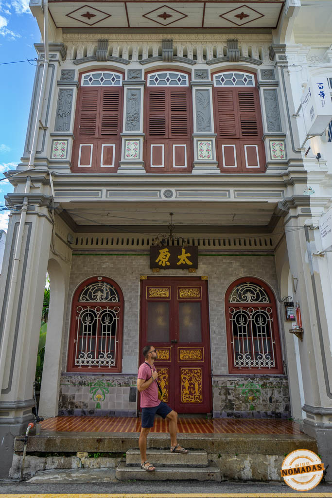 Viajero observando la espectacular fachada ornamentada de una tradicional shophouse restaurada con puertas rojas y detalles dorados en el centro histórico de Georgetown, Penang.